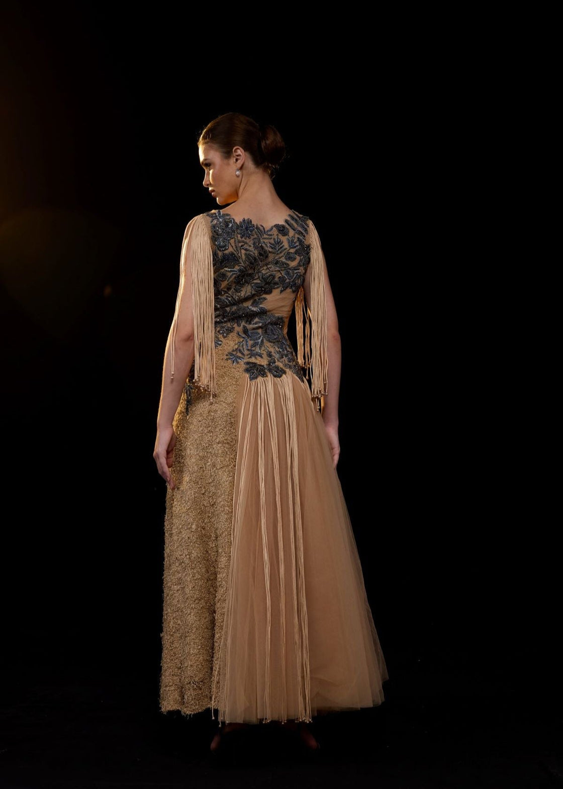 A nude toned gown adorned with intricate blue floral embroidery and dramatic fringe sleeves.