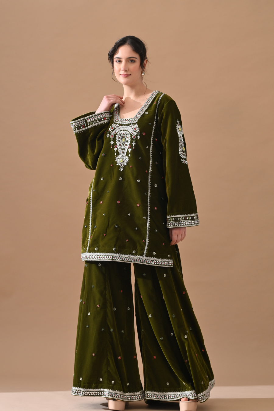 Woman wearing a green embroidered traditional outfit on a beige background