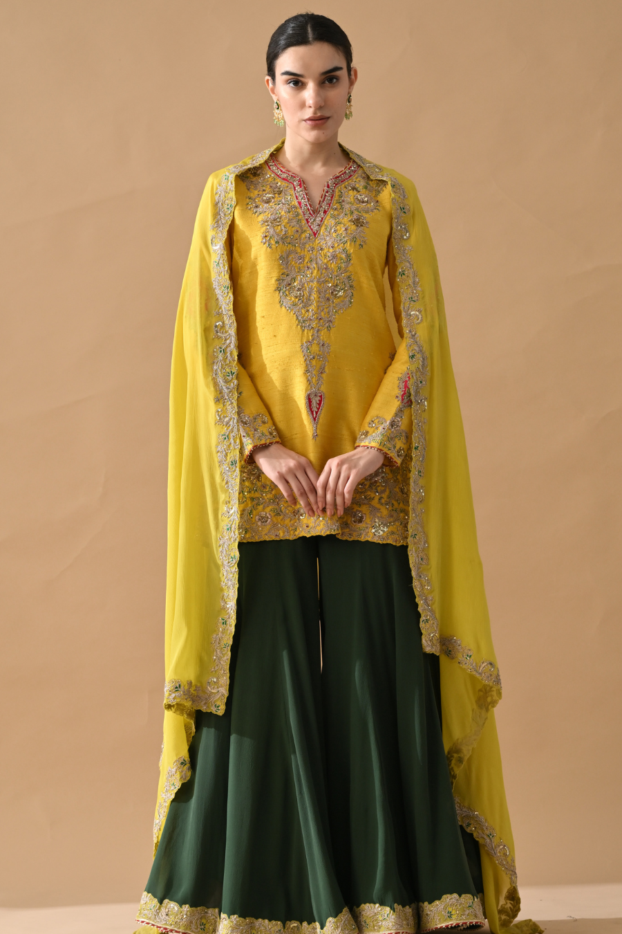 Woman wearing a yellow and green traditional outfit with embroidery on a beige background