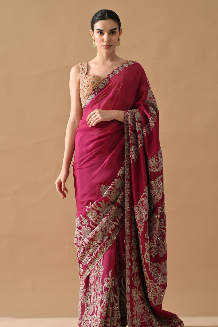 Woman wearing a pink saree with intricate patterns on a beige background