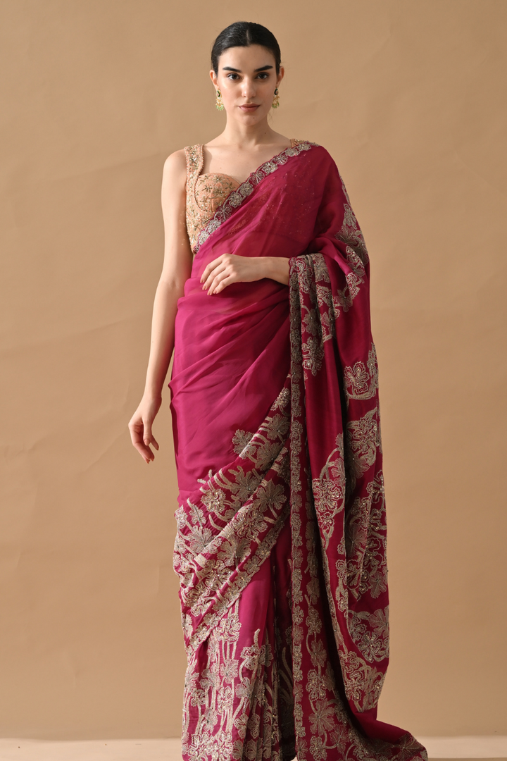 Woman wearing a pink saree with intricate patterns on a beige background
