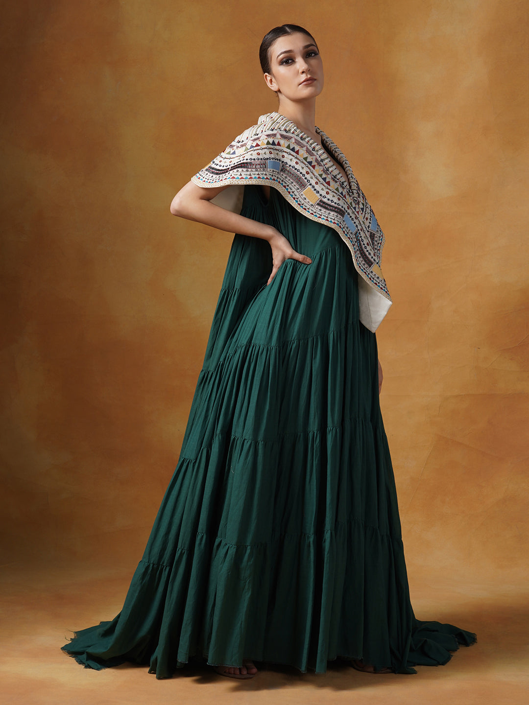 Floor length cotton tier dress in olive green. It is topped with a heavy embroidered cape around the neckline and shoulders.