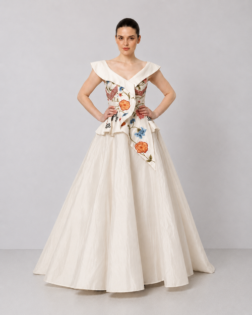 Ivory floral embroidered peplum gown with an off-shoulder neckline and voluminous drape.