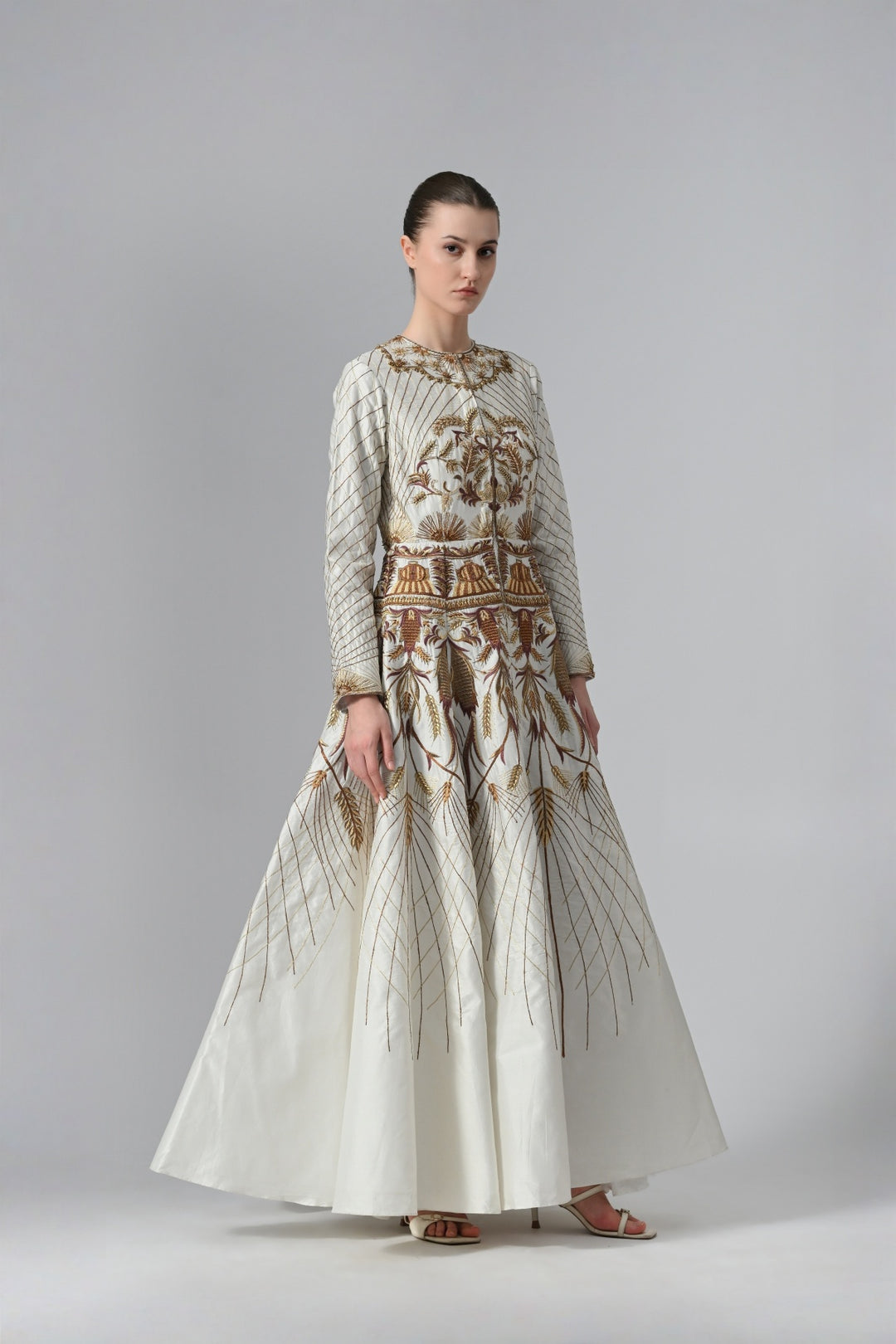 Ivory embroidered A-line gown featuring elegant round neckline, full-sleeves, structured bodice, and the gown is adorned with intricate botanical &amp; heritage-inspired motifs.