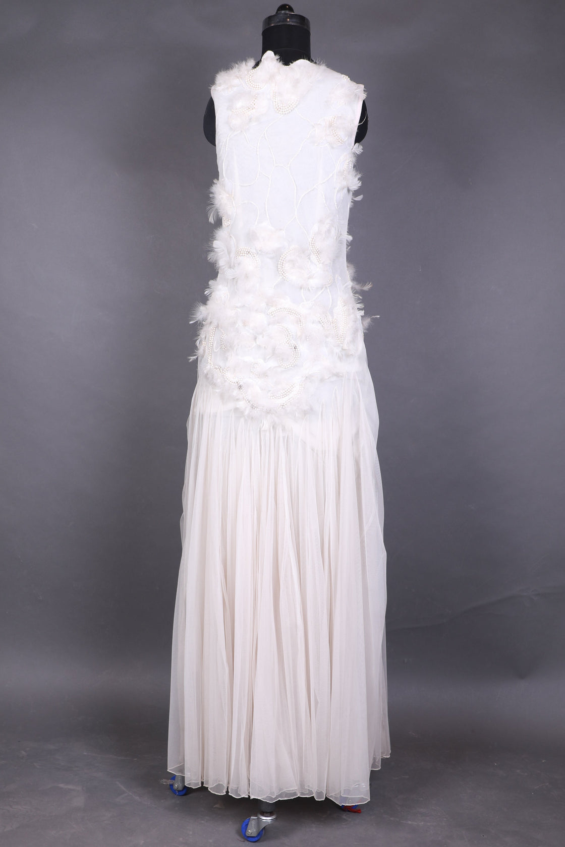 White evening gown with floral details on a mannequin against a dark background