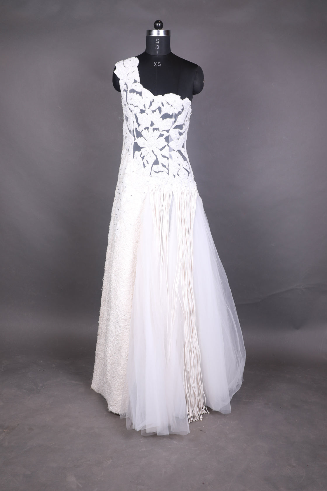 This one-shoulder ivory gown features intricate floral appliqué with sheer paneling