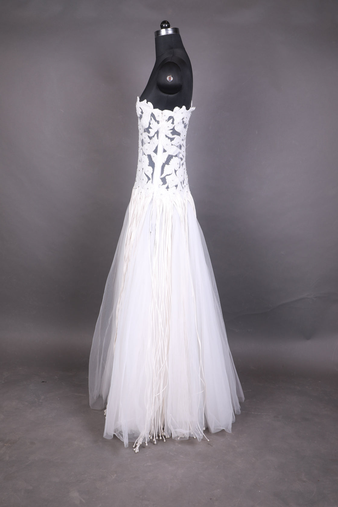 This one-shoulder ivory gown features intricate floral appliqué with sheer paneling