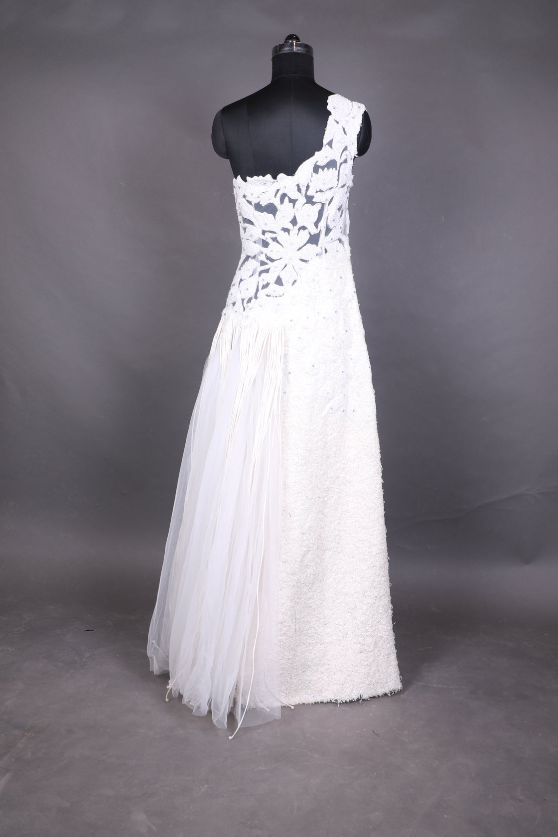 This one-shoulder ivory gown features intricate floral appliqué with sheer paneling