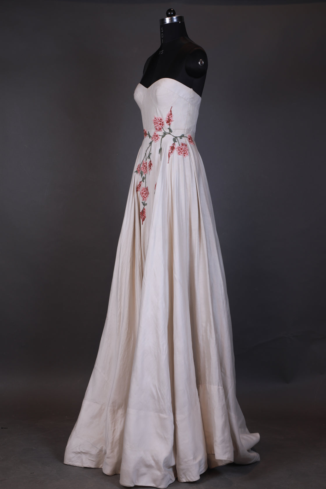 White dress with red floral embroidery on a mannequin against a dark background