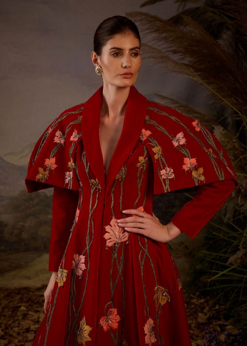 A red velvet fabric floor length gown with lapel neck line & extended cape