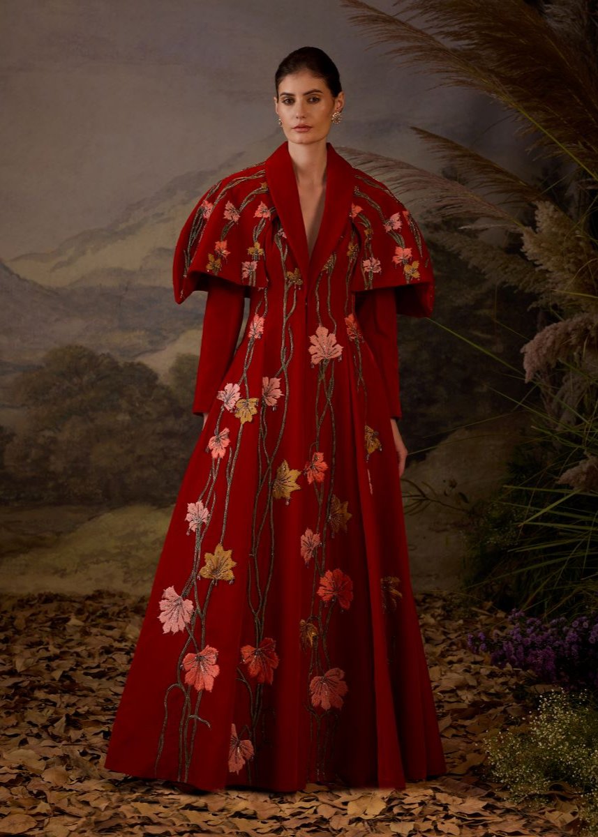 A red velvet fabric floor length gown with lapel neck line & extended cape