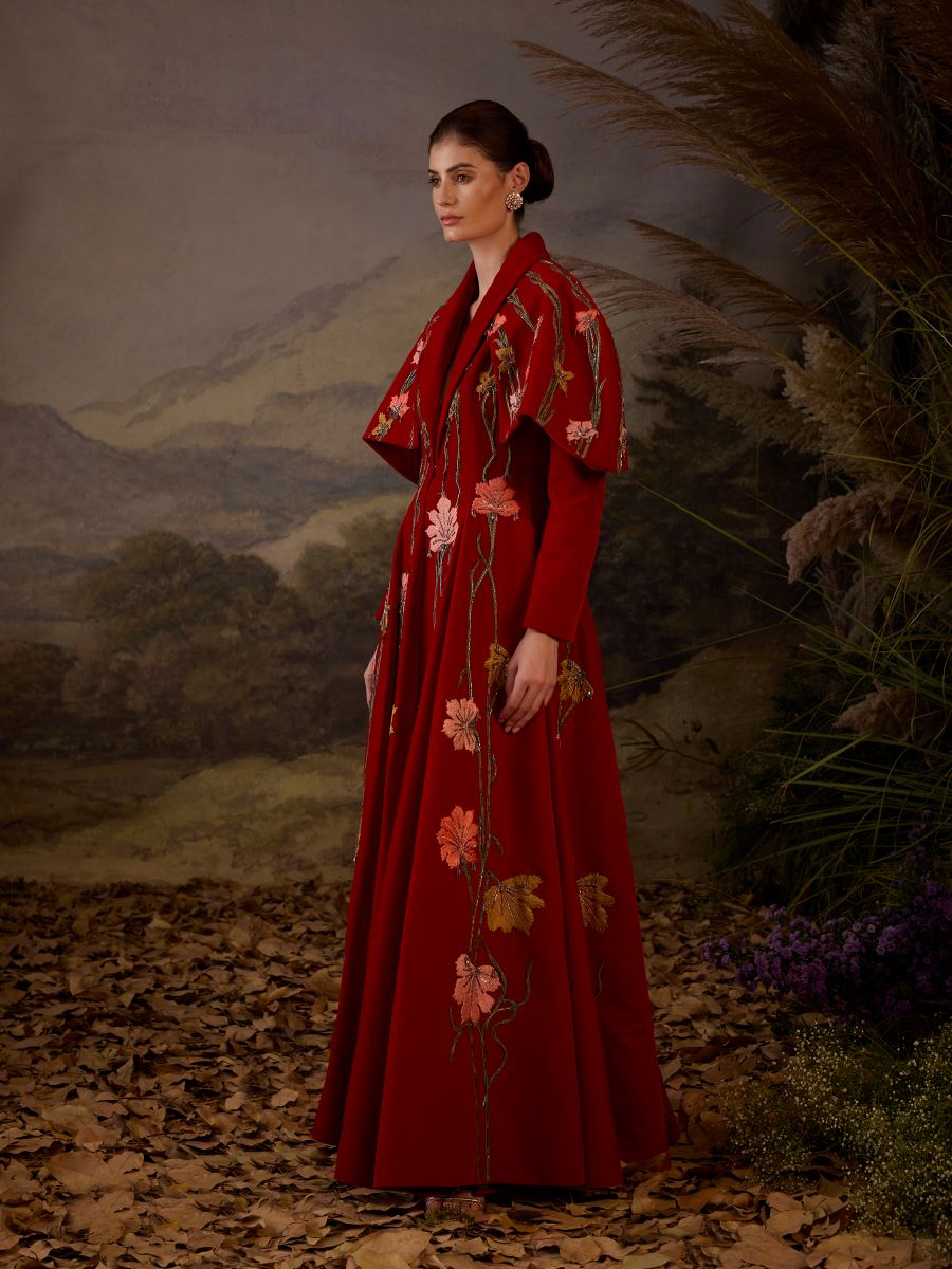 A red velvet fabric floor length gown with lapel neck line & extended cape