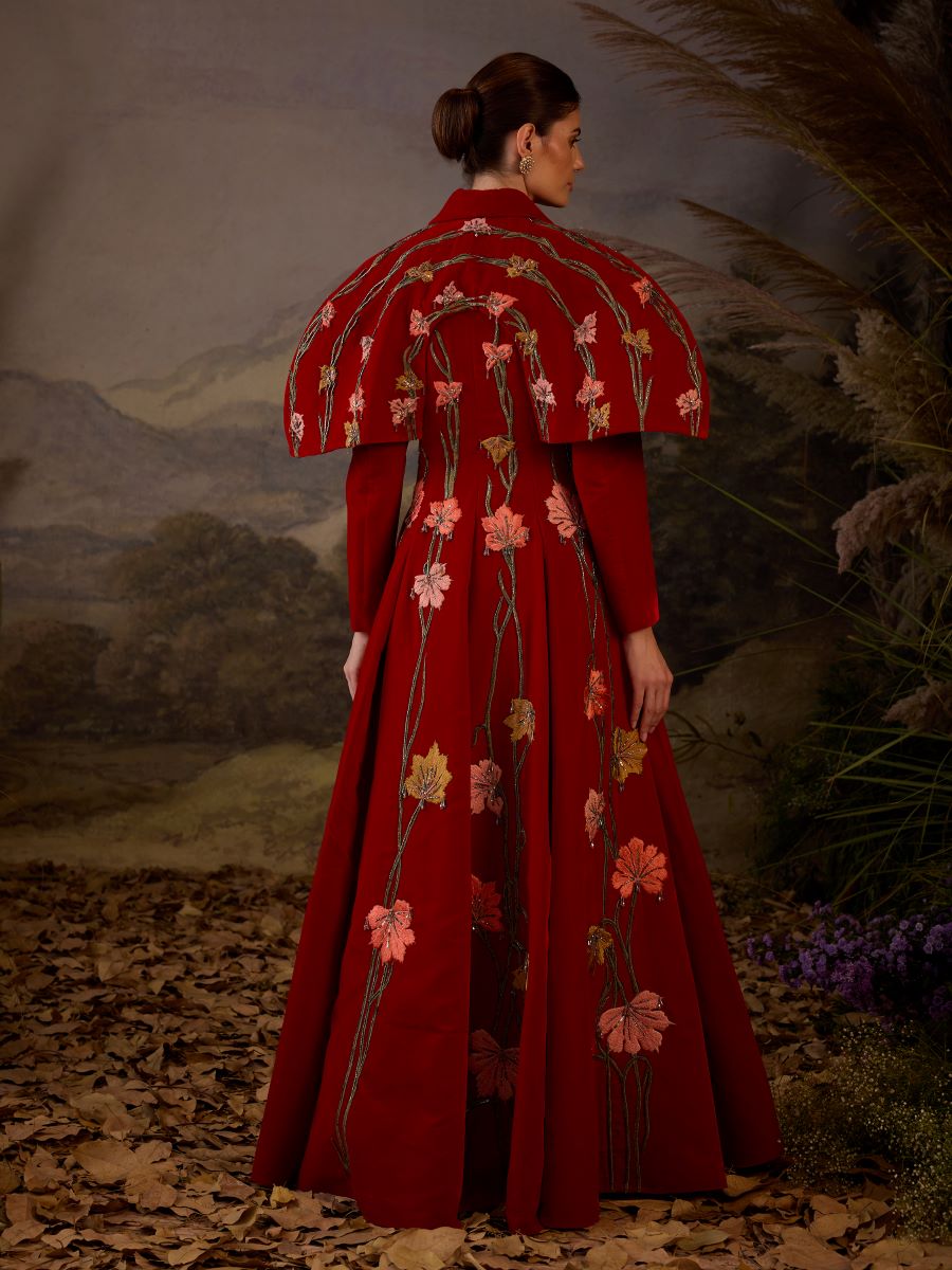 A red velvet fabric floor length gown with lapel neck line & extended cape