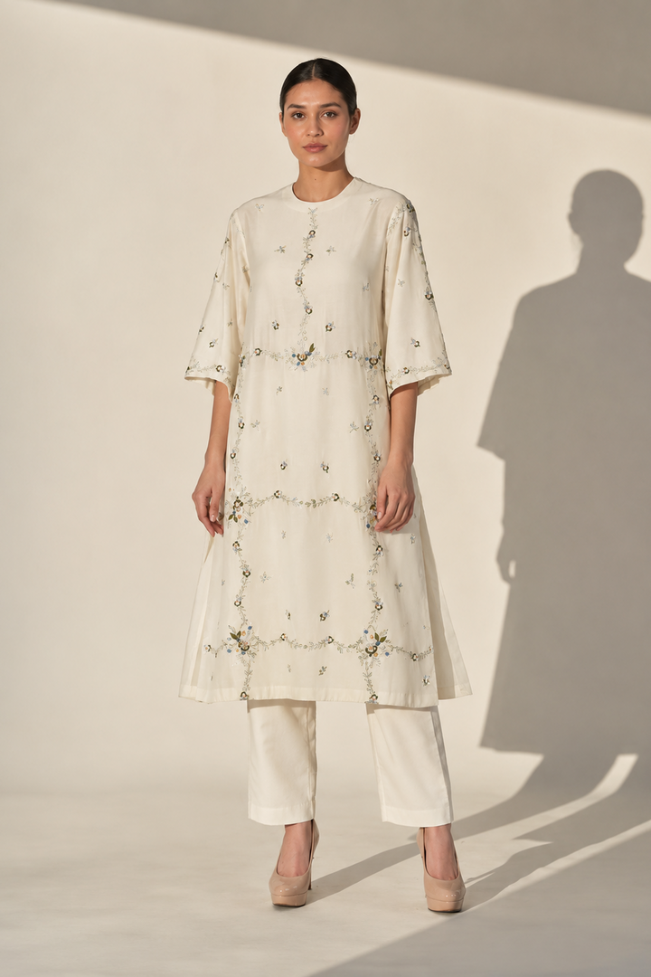 Woman wearing a cream-colored outfit with floral embroidery against a white background