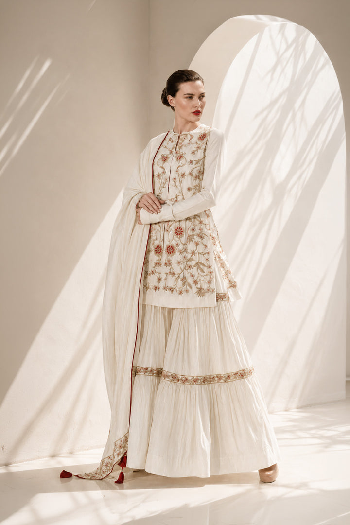 Ivory kurta set adorned with delicate floral embroidery, paired with a tiered sharara and embroidered dupatta.