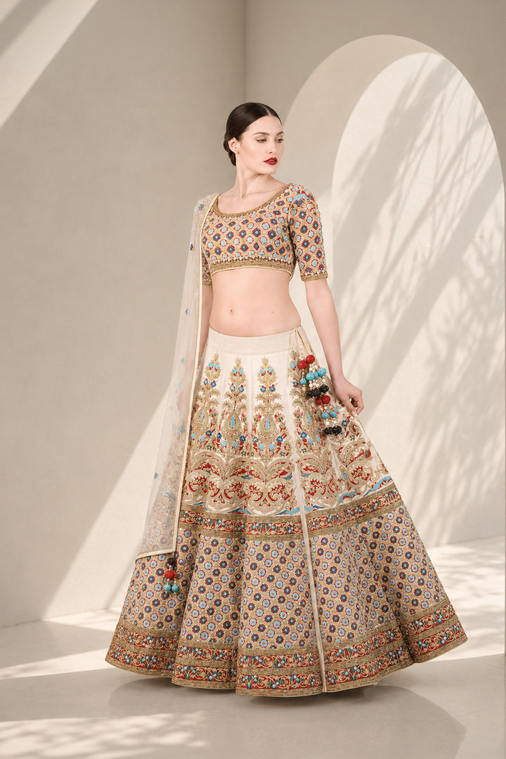 Ivory lehenga set featuring boat neckline blouse with elbow-length sleeves &amp; adorned with inrticate multicolor embroidery, paired with richly embellished skirt &amp; sheer dupatta.