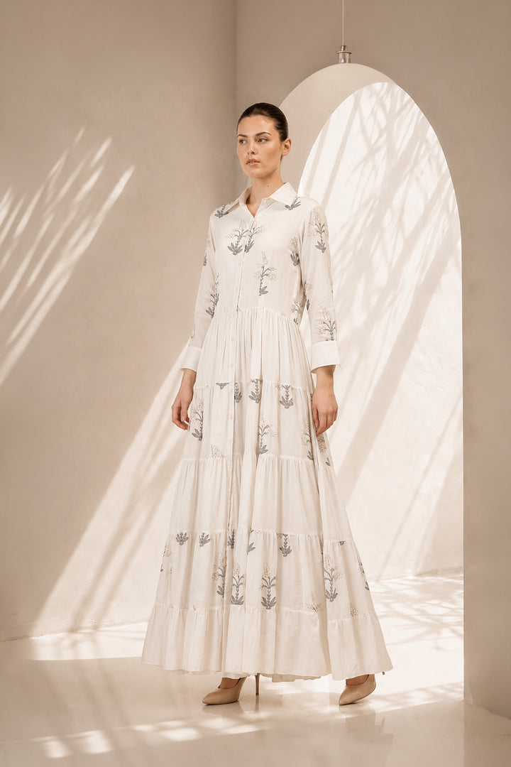 Ivory shirt dress adorned with delicate botanical prints, featuring a structured collar and cascading tiered silhouette.