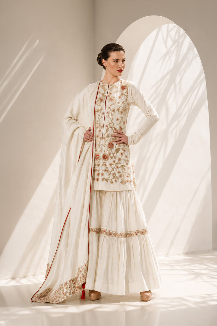 Ivory kurta set adorned with delicate floral embroidery, paired with a tiered sharara and embroidered dupatta.