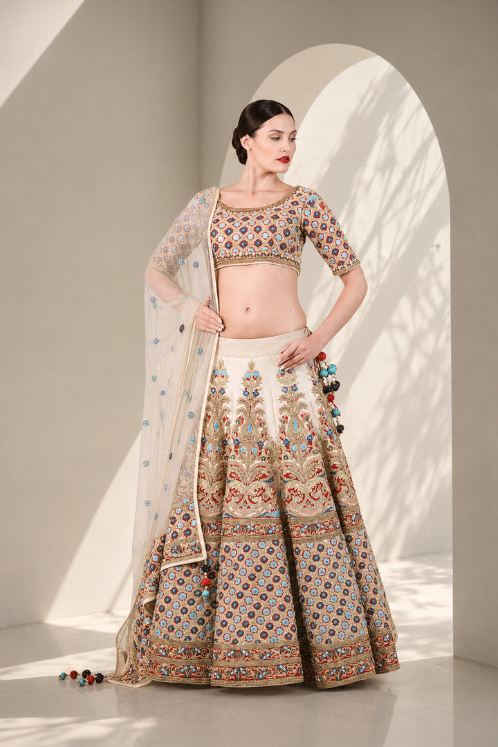 Ivory lehenga set featuring boat neckline blouse with elbow-length sleeves &amp; adorned with inrticate multicolor embroidery, paired with richly embellished skirt &amp; sheer dupatta.