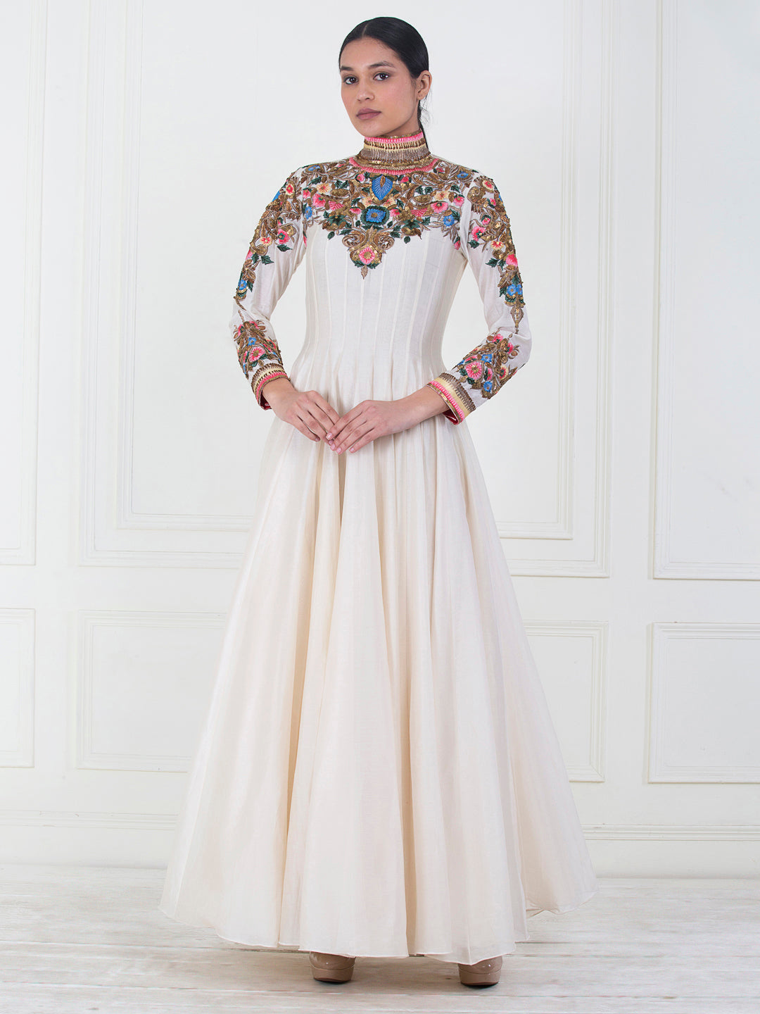 Woman wearing a long, white dress with floral embroidery on a white background