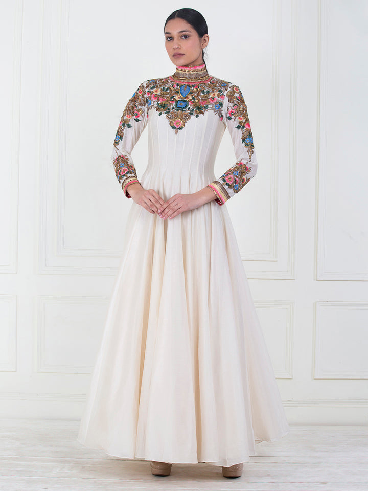 Woman wearing a long, white dress with floral embroidery on a white background