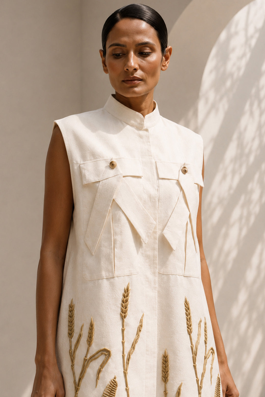 Ivory modern sleeveless statement dress featuring sculptural pocket detailing and intricate wheat-inspired embroidery.