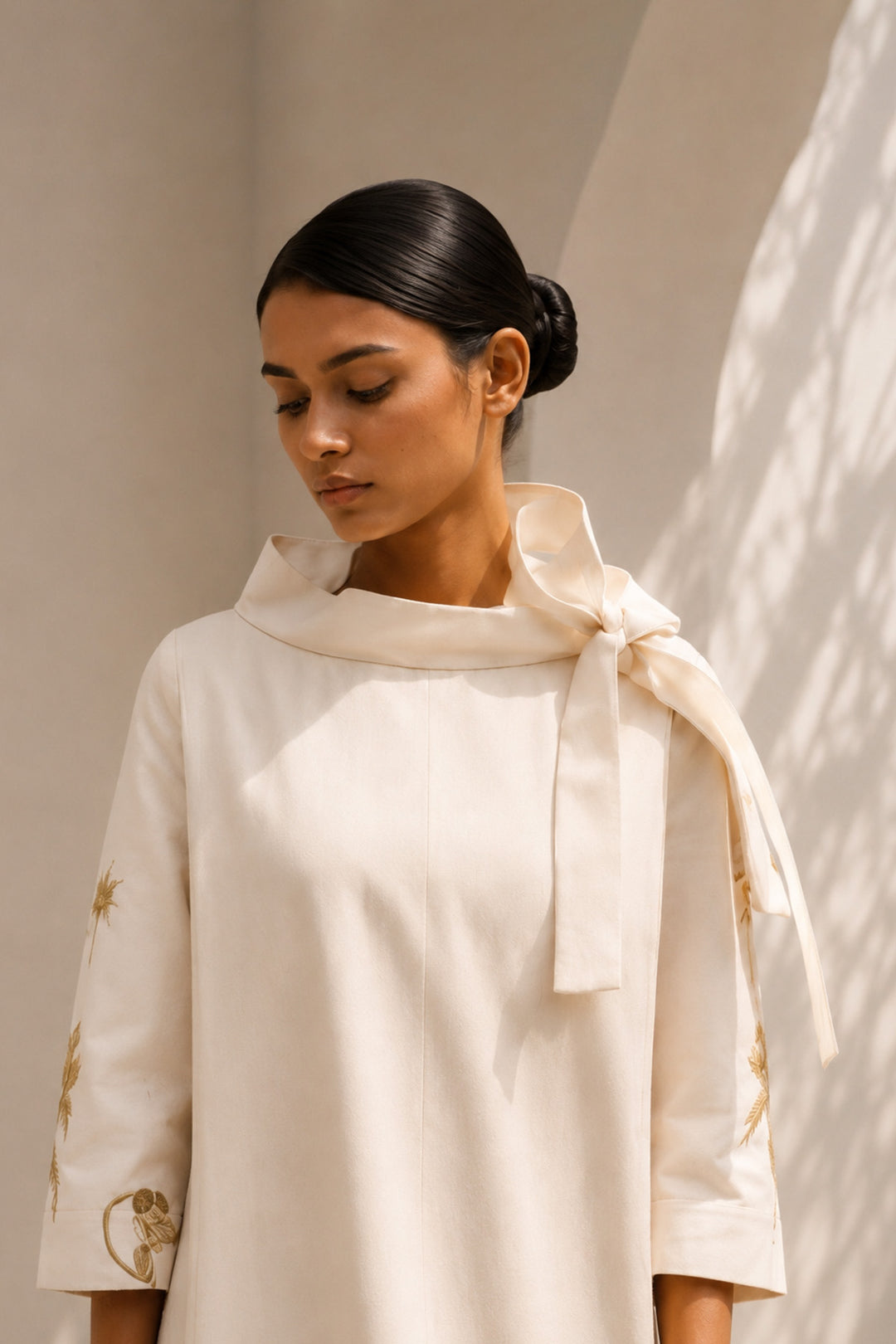 Ivory shift dress adorned with bold botanical artwork and a sculptural bow neckline.