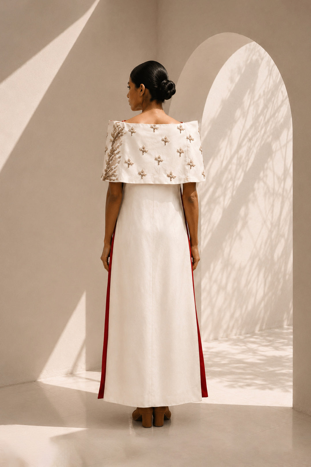 Ivory striking architectural ensemble featuring a sculptural cape overlay, dramatic side panels, and contrasting crimson accents that redefine contemporary elegance.