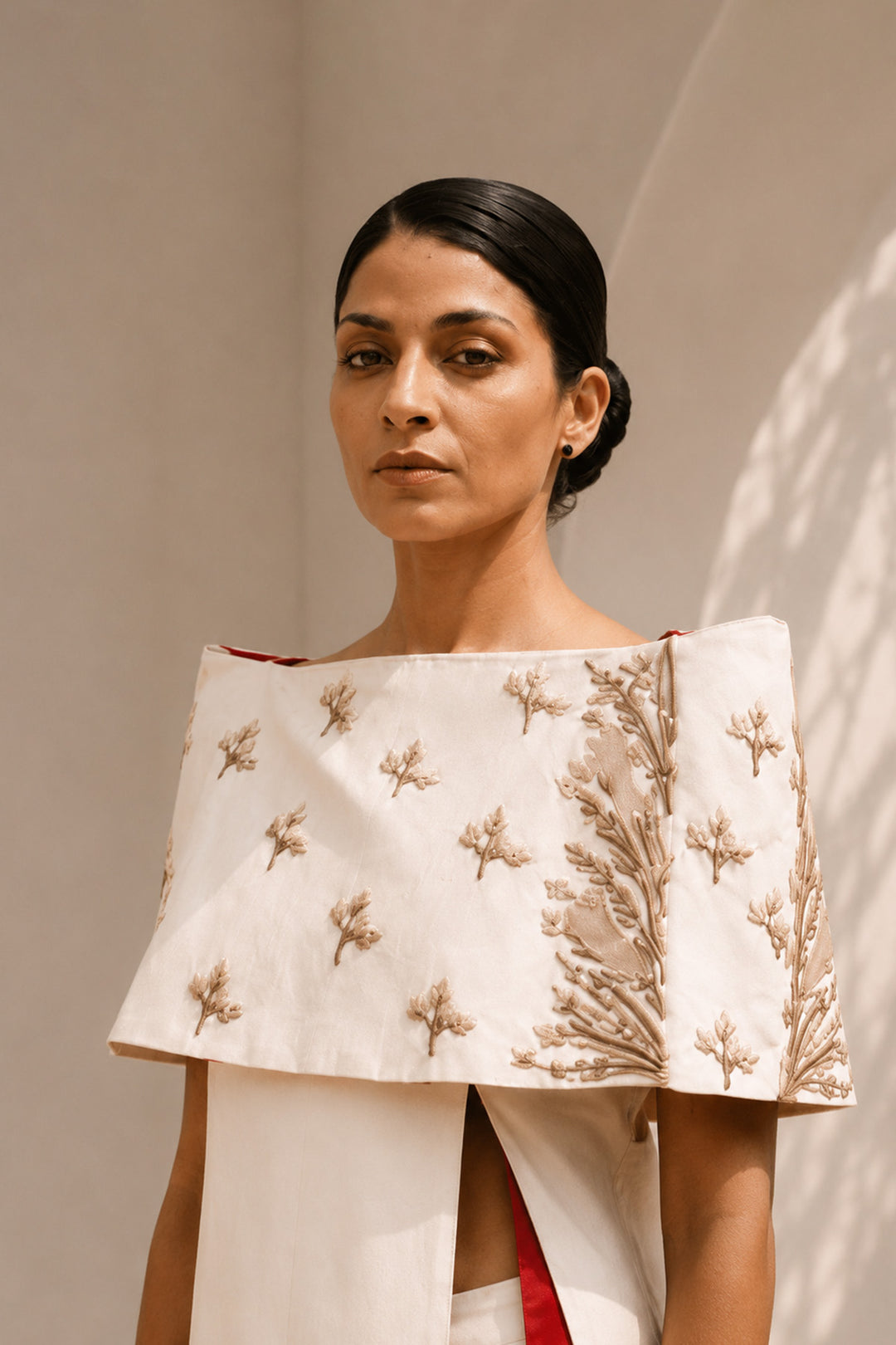 Ivory striking architectural ensemble featuring a sculptural cape overlay, dramatic side panels, and contrasting crimson accents that redefine contemporary elegance.
