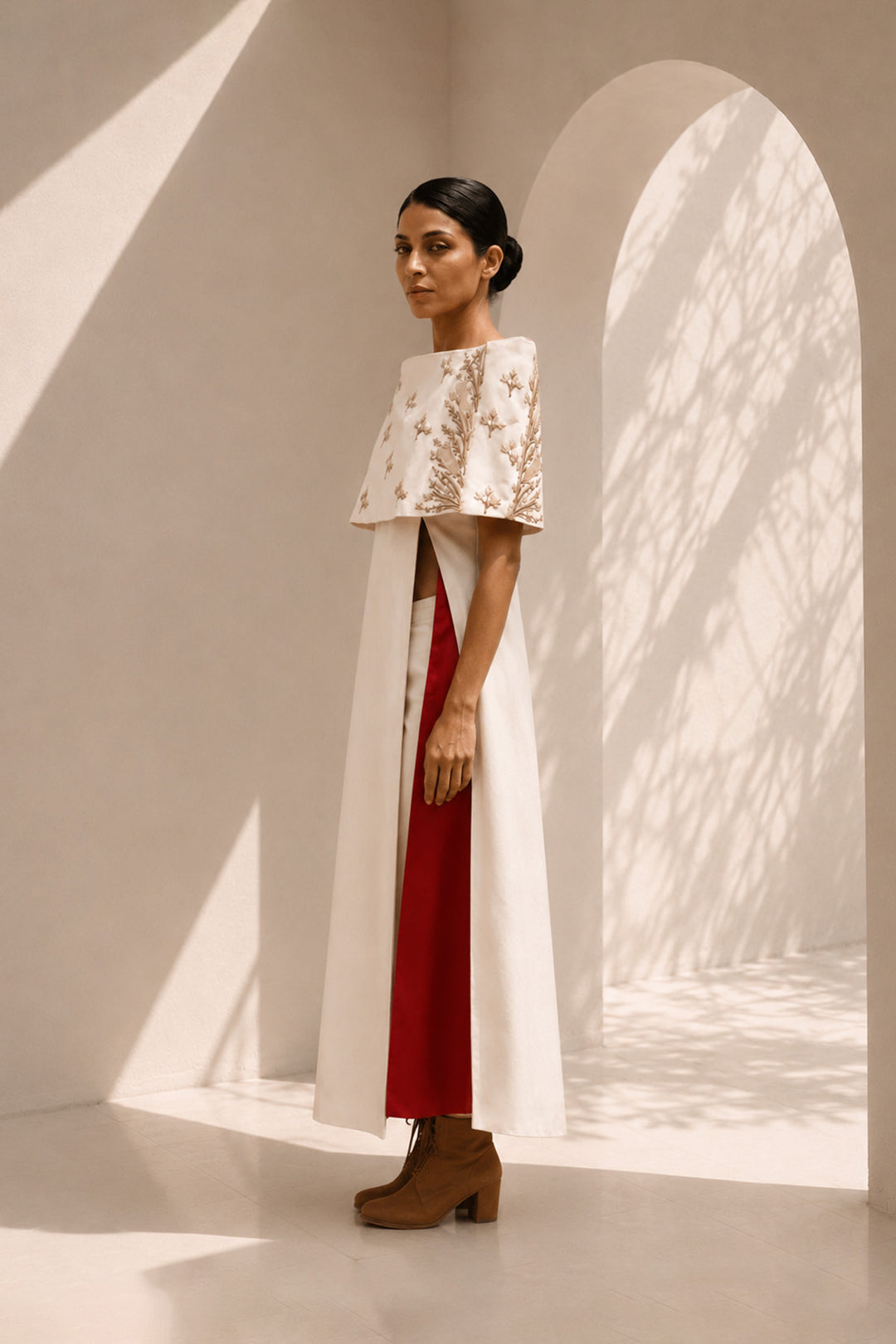 Ivory striking architectural ensemble featuring a sculptural cape overlay, dramatic side panels, and contrasting crimson accents that redefine contemporary elegance.