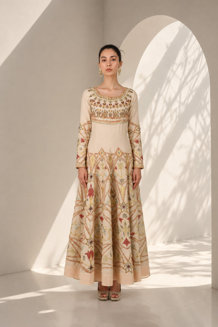 Ivory embroidered gown adorned with intricate geometric and floral motifs, featuring fitted bodice, full sleeves and a voluminous flared hem.