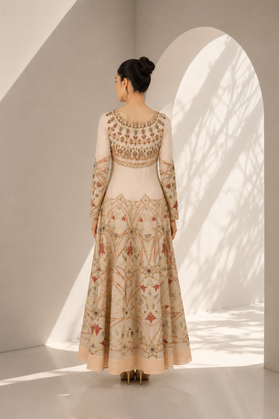 Ivory embroidered gown adorned with intricate geometric and floral motifs, featuring fitted bodice, full sleeves and a voluminous flared hem.