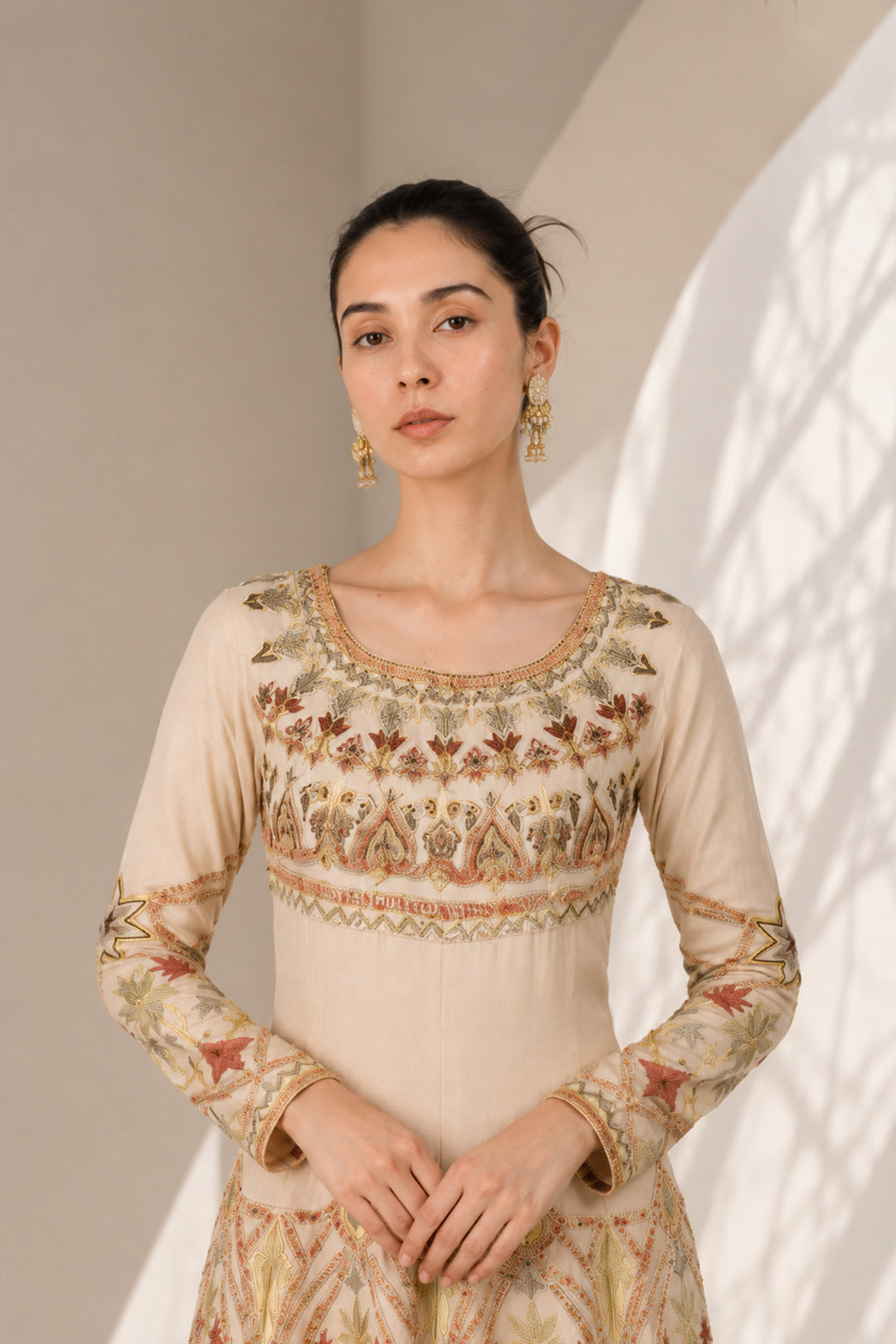 Ivory embroidered gown adorned with intricate geometric and floral motifs, featuring fitted bodice, full sleeves and a voluminous flared hem.