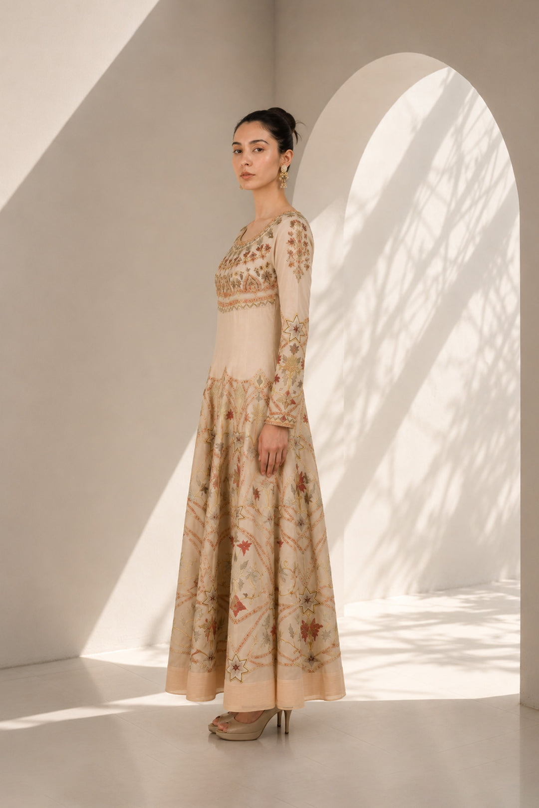 Ivory embroidered gown adorned with intricate geometric and floral motifs, featuring fitted bodice, full sleeves and a voluminous flared hem.