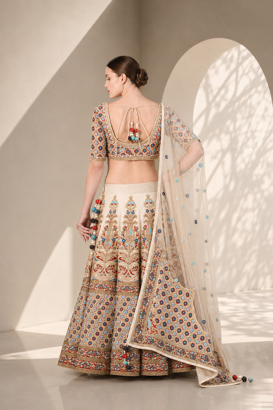 Ivory lehenga set featuring boat neckline blouse with elbow-length sleeves &amp; adorned with inrticate multicolor embroidery, paired with richly embellished skirt &amp; sheer dupatta.