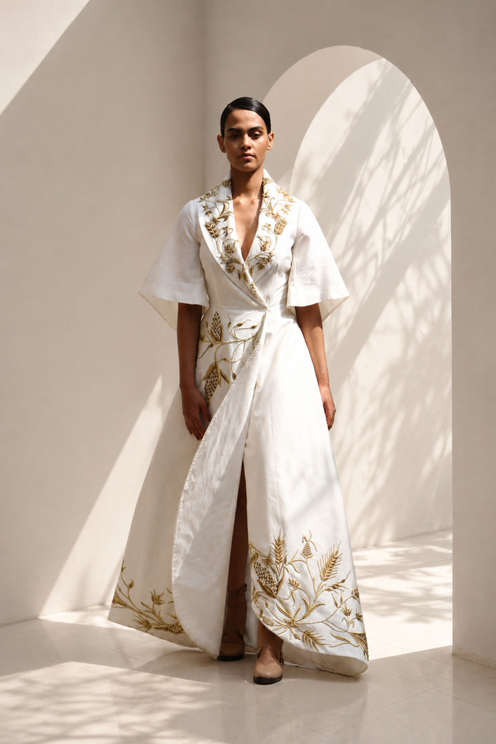Ivory wrap gown adorned with intricate embroidery, featuring shawl collar and flared sleeves, blending contemporary tailoring with timeless artisanal craftsmanship.