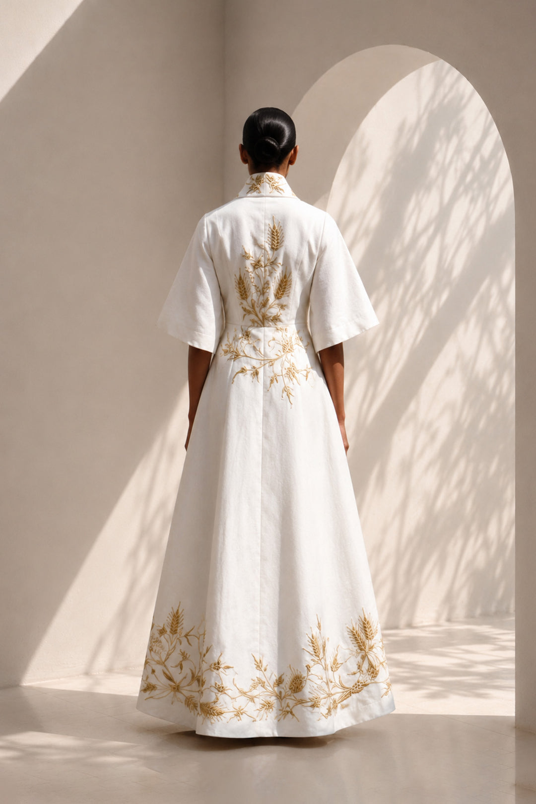 Ivory wrap gown adorned with intricate embroidery, featuring shawl collar and flared sleeves, blending contemporary tailoring with timeless artisanal craftsmanship.