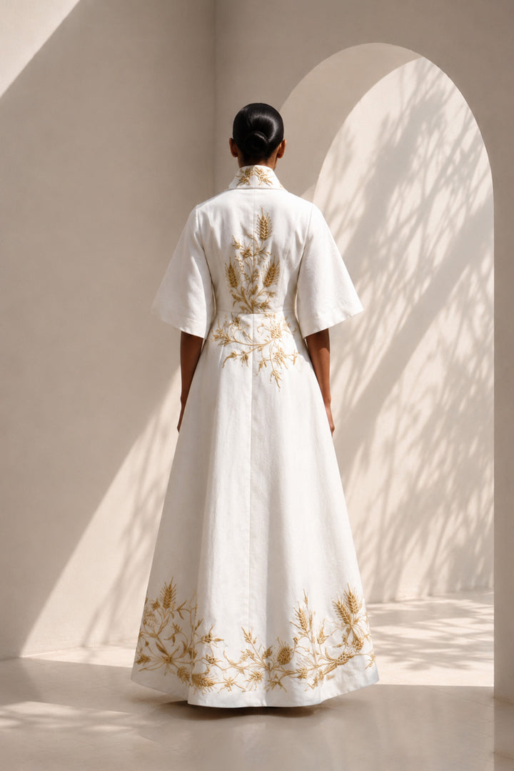 Ivory wrap gown adorned with intricate embroidery, featuring shawl collar and flared sleeves, blending contemporary tailoring with timeless artisanal craftsmanship.