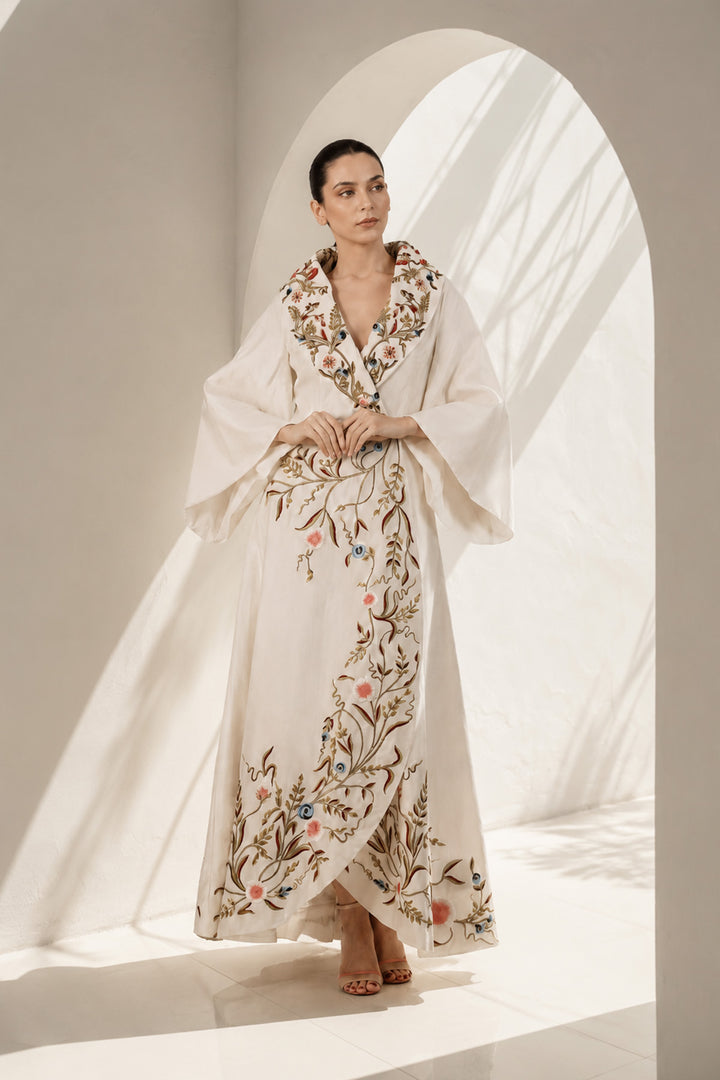 Ivory wrap gown adorned with embroidery, featuring shawl collar neckline,  bell sleeves and fluid drape.