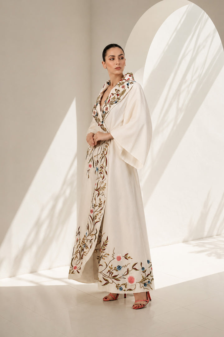 Ivory wrap gown adorned with embroidery, featuring shawl collar neckline,  bell sleeves and fluid drape.