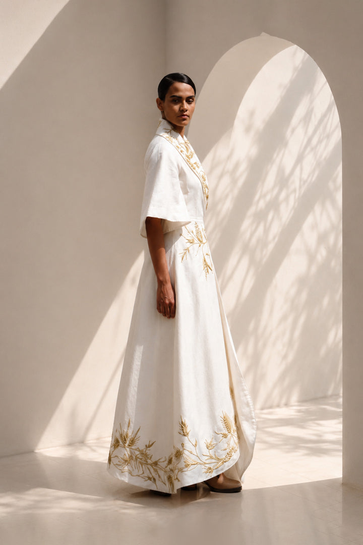Ivory wrap gown adorned with intricate embroidery, featuring shawl collar and flared sleeves, blending contemporary tailoring with timeless artisanal craftsmanship.
