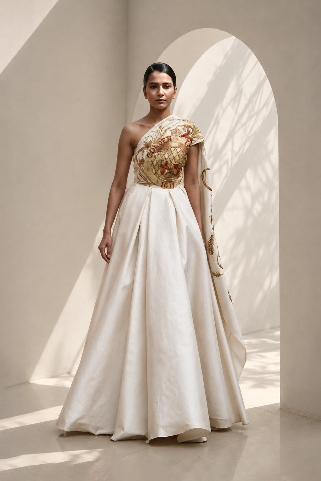 Ivory statement shoulder panel gown featuring gold and crimson artwork and sculptural draping.