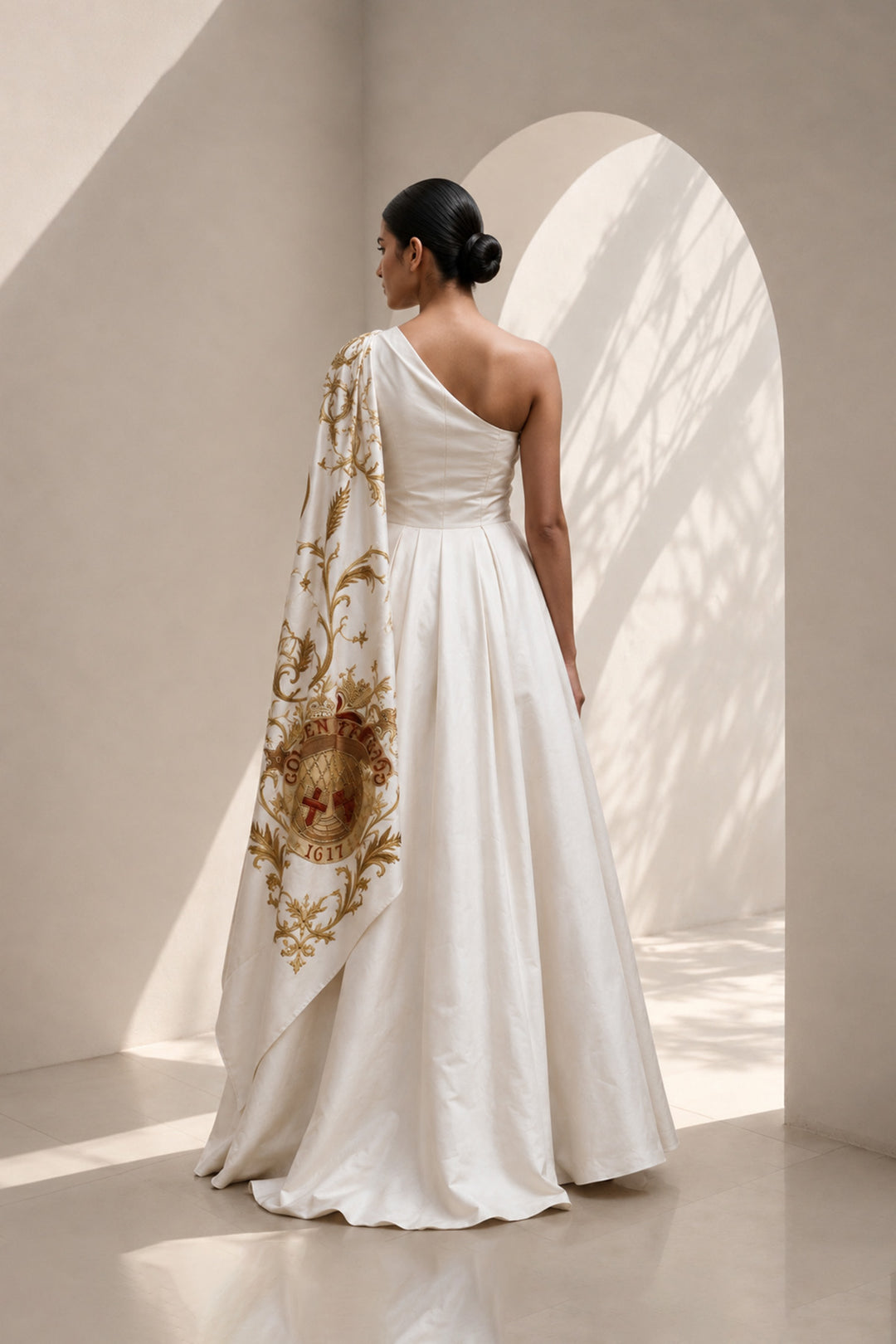Ivory statement shoulder panel gown featuring gold and crimson artwork and sculptural draping.