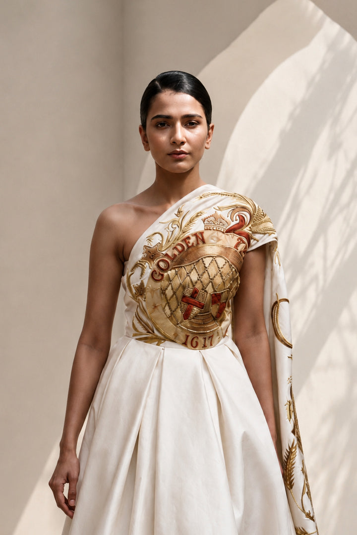 Ivory statement shoulder panel gown featuring gold and crimson artwork and sculptural draping.
