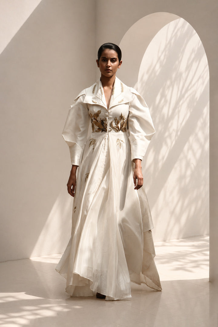 Ivory statement gown featuring sculptural sleeves, delicate embroidery, and an effortlessly flowing silhouette.