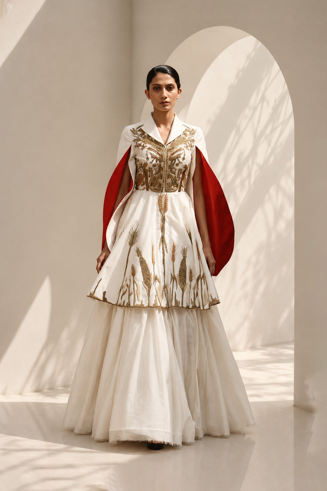Ivory ensemble featuring intricate gold embroidery, dramatic cape sleeves, and layered volume for a look that is both regal and contemporary.