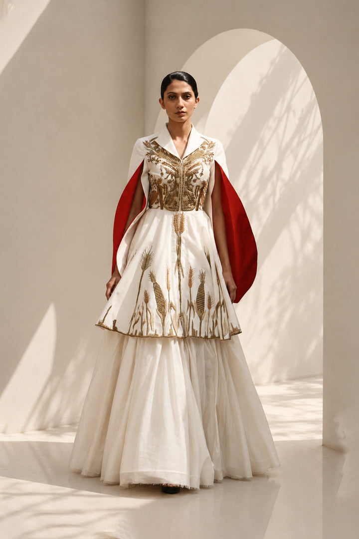 Ivory ensemble featuring intricate gold embroidery, dramatic cape sleeves, and layered volume for a look that is both regal and contemporary.