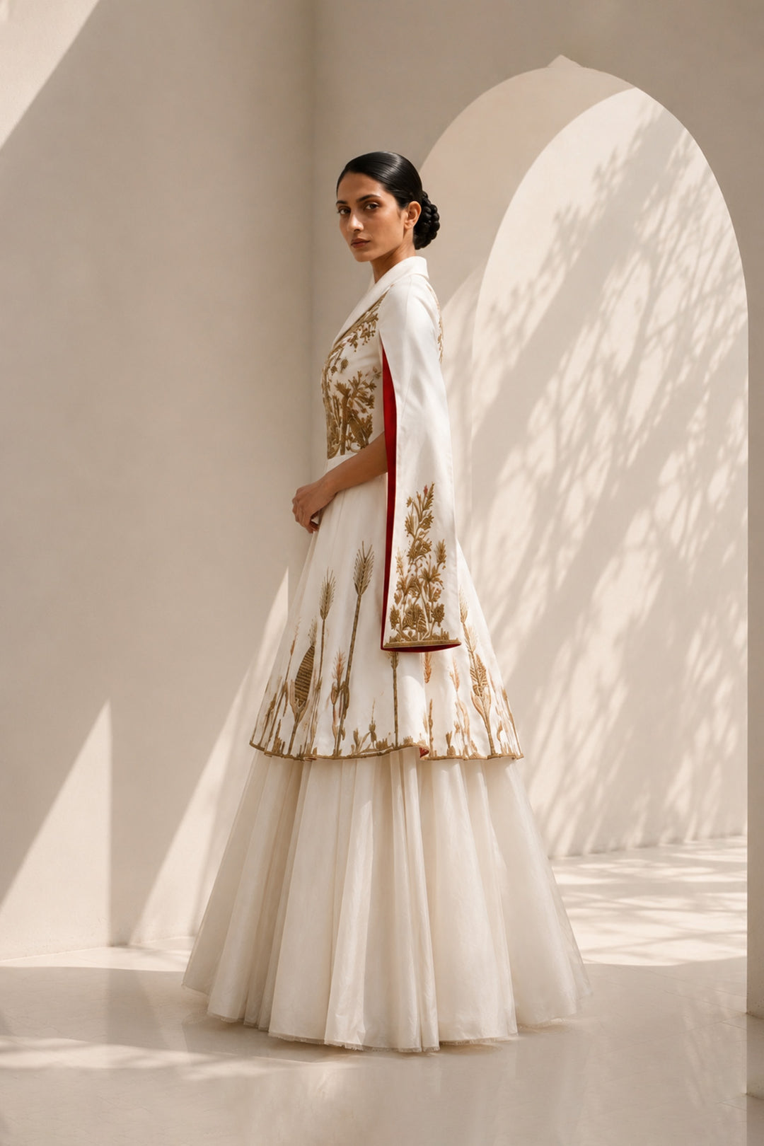 Ivory ensemble featuring intricate gold embroidery, dramatic cape sleeves, and layered volume for a look that is both regal and contemporary.