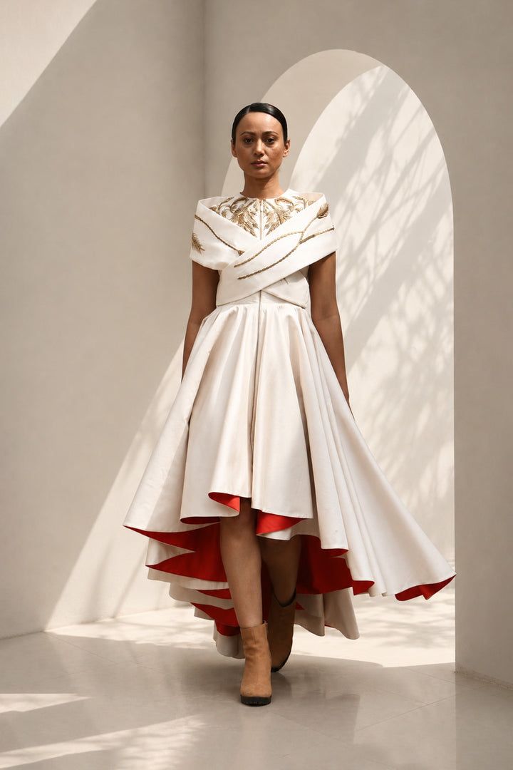 Ivory high-low dress featuring sculptural draped detailing, delicate embroidery, and a striking scarlet contrast lining for a bold yet refined statement.
