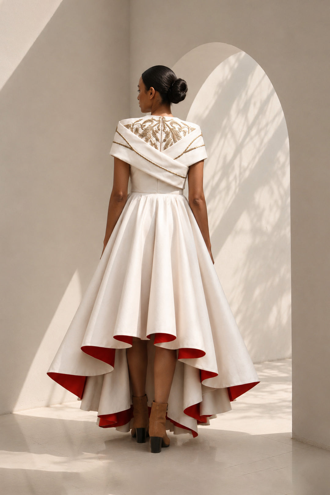 Ivory high-low dress featuring sculptural draped detailing, delicate embroidery, and a striking scarlet contrast lining for a bold yet refined statement.